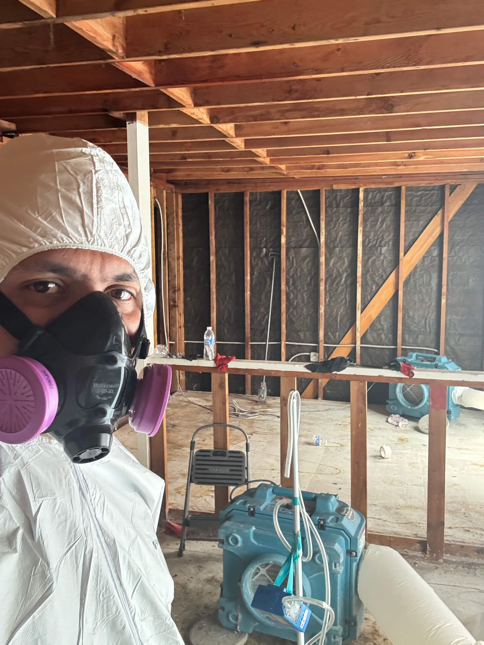 Professional technician in protective gear monitoring an asbestos abatement site with air filtration equipment.