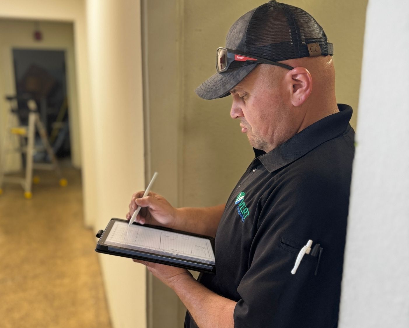 user-inserted Asbestos inspector documenting findings on a tablet during an indoor field inspection, wearing protective gear and company uniform while recording compliance information