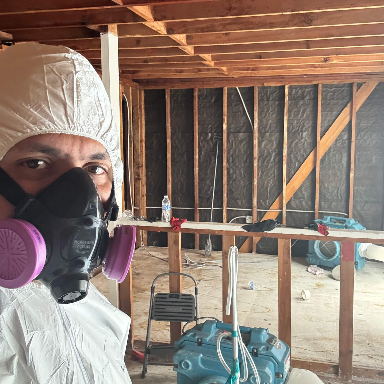 Professional technician in protective gear monitoring an asbestos abatement site with air filtration equipment.